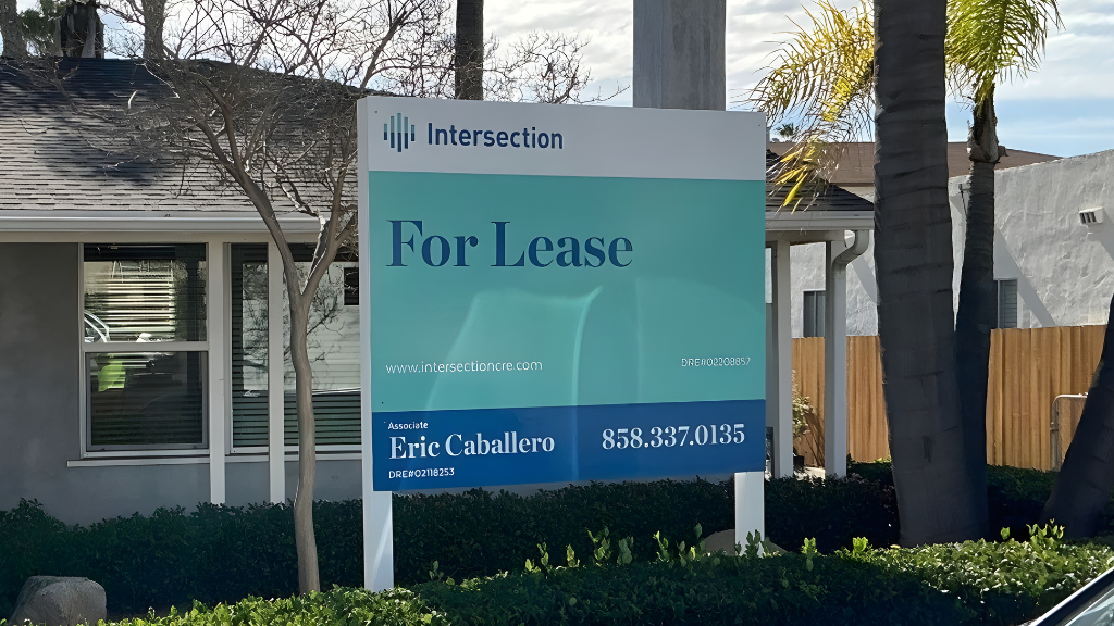 Commercial building with a “For Lease” real estate sign by Intersection displaying agent Eric Caballero and phone number in front of landscaped property.