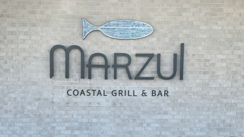  Marzul Coastal Grill & Bar sign with fish logo mounted on a light brick wall