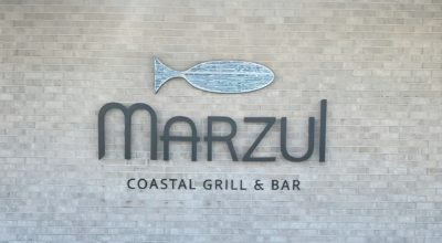 Marzul Coastal Grill & Bar sign with fish logo mounted on a light brick wall