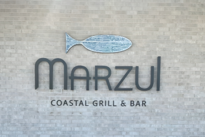 Marzul Coastal Grill & Bar sign with fish logo mounted on a light brick wall