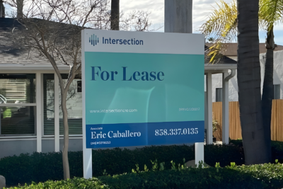 Commercial building with a “For Lease” real estate sign by Intersection displaying agent Eric Caballero and phone number in front of landscaped property.
