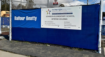 Construction site fencing with Balfour Beatty banner and Johnson Elementary School interim housing signage in San Diego