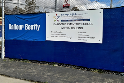 Construction site fencing with Balfour Beatty banner and Johnson Elementary School interim housing signage in San Diego