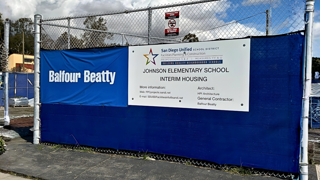 Construction site fencing with Balfour Beatty banner and Johnson Elementary School interim housing signage in San Diego