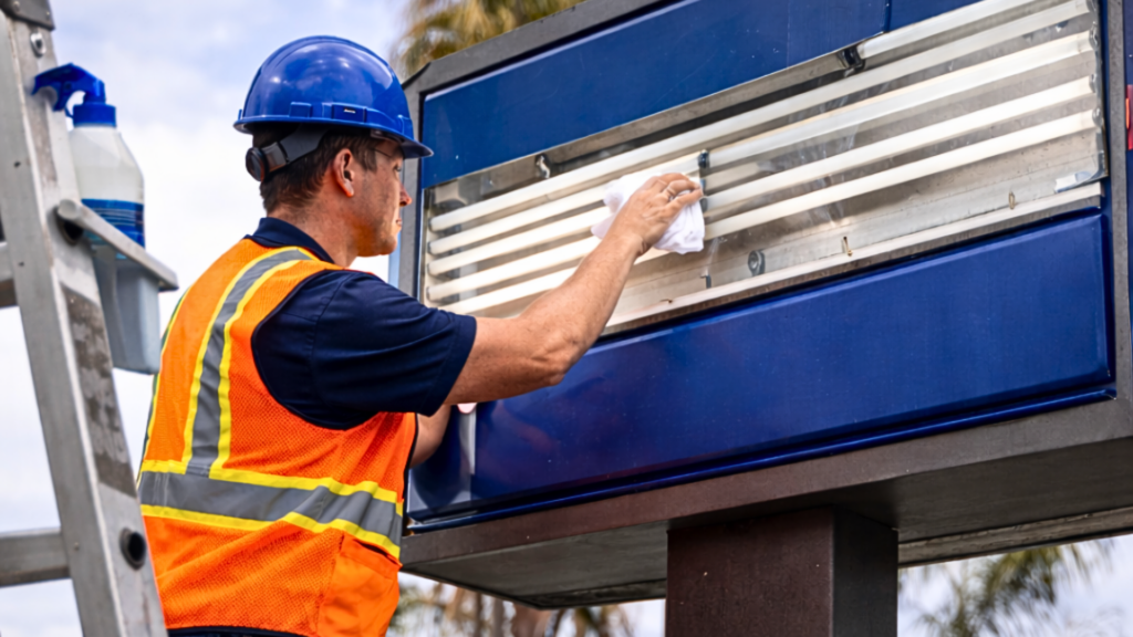 Sign technician cleaning and maintaining an outdoor illuminated sign on a ladder in San Diego