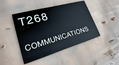 Black ADA-compliant room identification sign with raised white tactile lettering reading "T268 Communications" for interior office wayfinding.