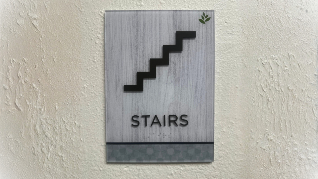 ADA-compliant stair wayfinding sign installed inside a healthcare facility in San Diego, featuring tactile lettering and accessible directional graphics.