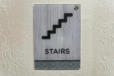ADA-compliant stair wayfinding sign installed inside a healthcare facility in San Diego, featuring tactile lettering and accessible directional graphics.