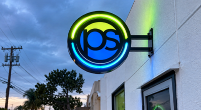 Circular LED illuminated projecting sign for Printing Solutions featuring blue and green lighting mounted on a commercial building in San Diego