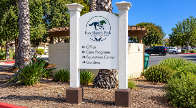 Custom wayfinding sign at Ivey Ranch Park Association with directional arrows guiding visitors to offices, care programs, equestrian center, and gardens